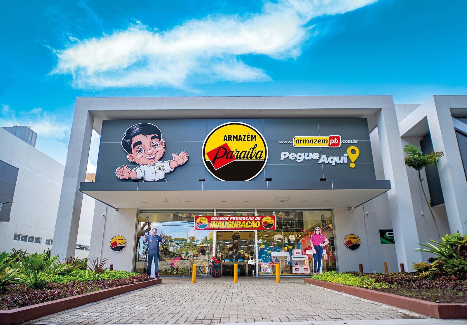 Loja moderna do Armazém Paraíba em João Pessoa, com fachada cinza, logotipo redondo amarelo, mascote ilustrado e faixa de inauguração