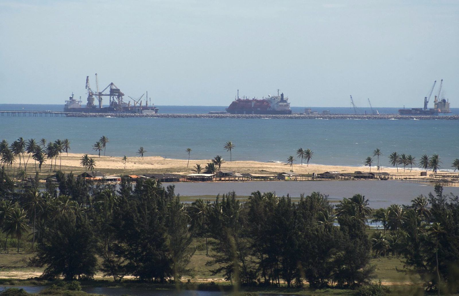 Navios atracados no píer do Porto do Pecém, com guindastes, vistos de longe sobre uma faixa de coqueiros e casuarinas