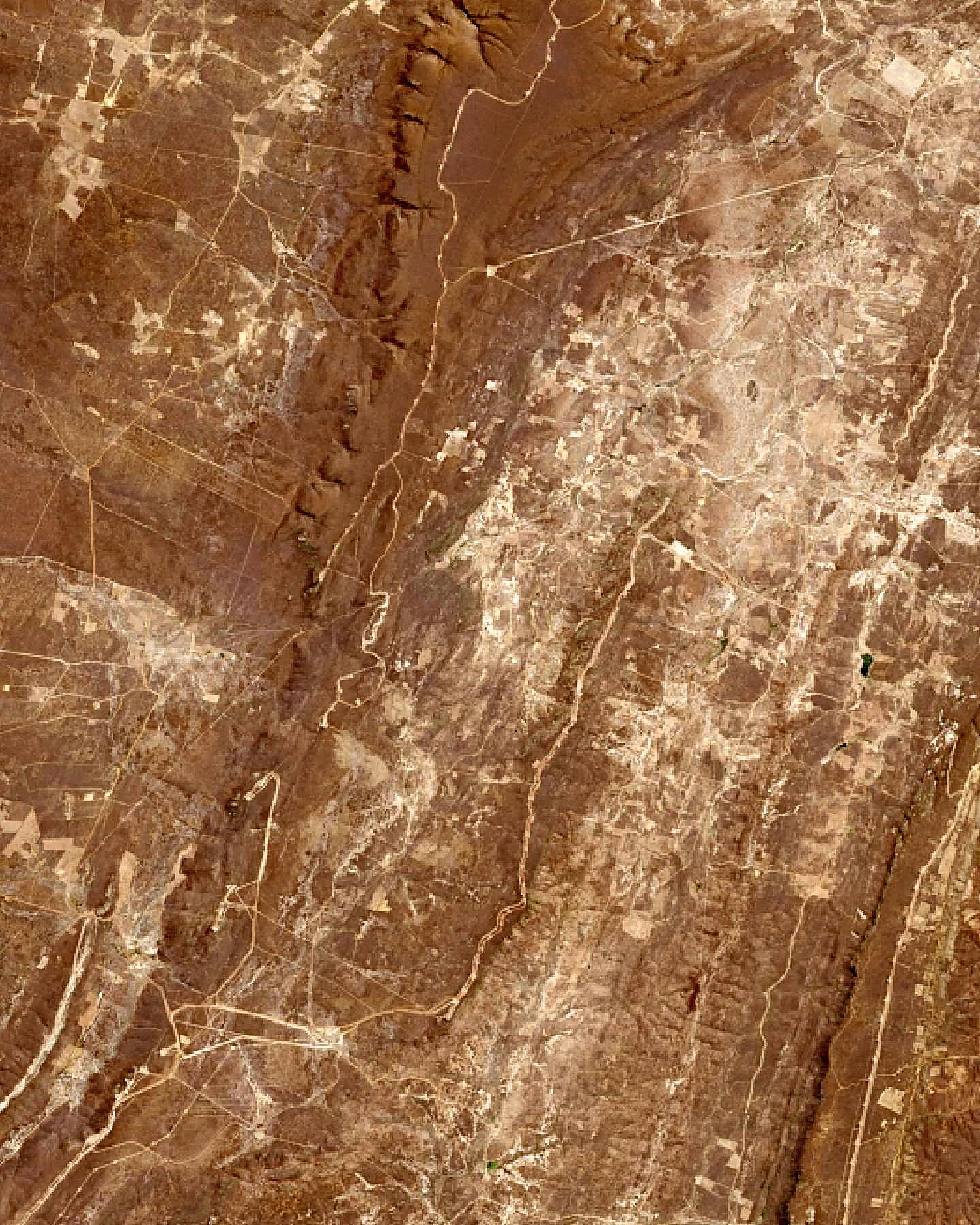 Imagem de satélite em cor natural de serras marrons na caatinga, cortadas por estradas de terra claras que levam às torres eólicas