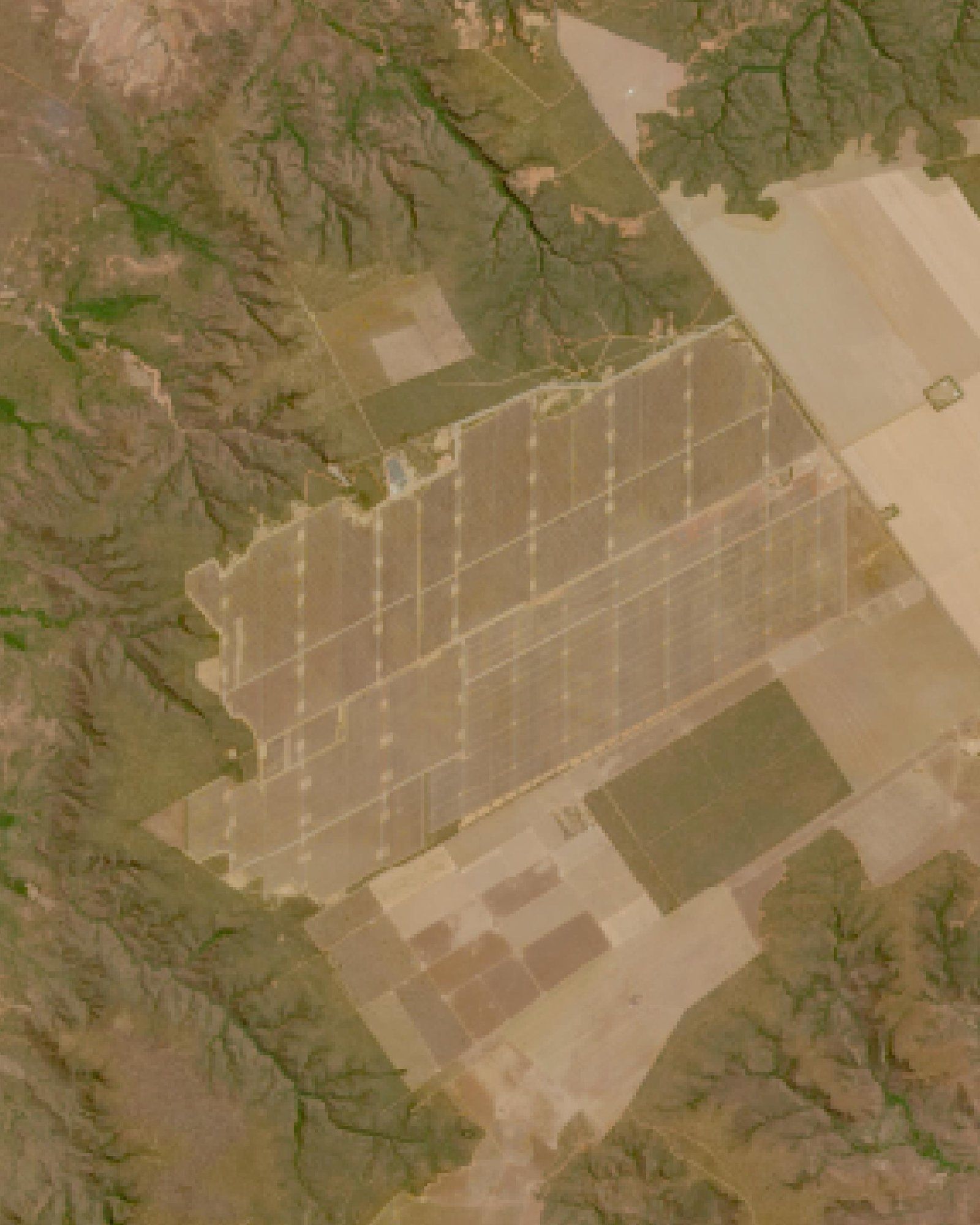 Imagem de satélite de um grande retângulo claro e quadriculado de painéis solares no meio do cerrado, cercado por vales verdes e lavouras