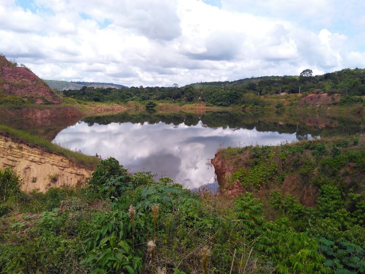 Lago da antiga cava do garimpo de Serra Pelada, com barrancos de terra vermelha e mata ao redor