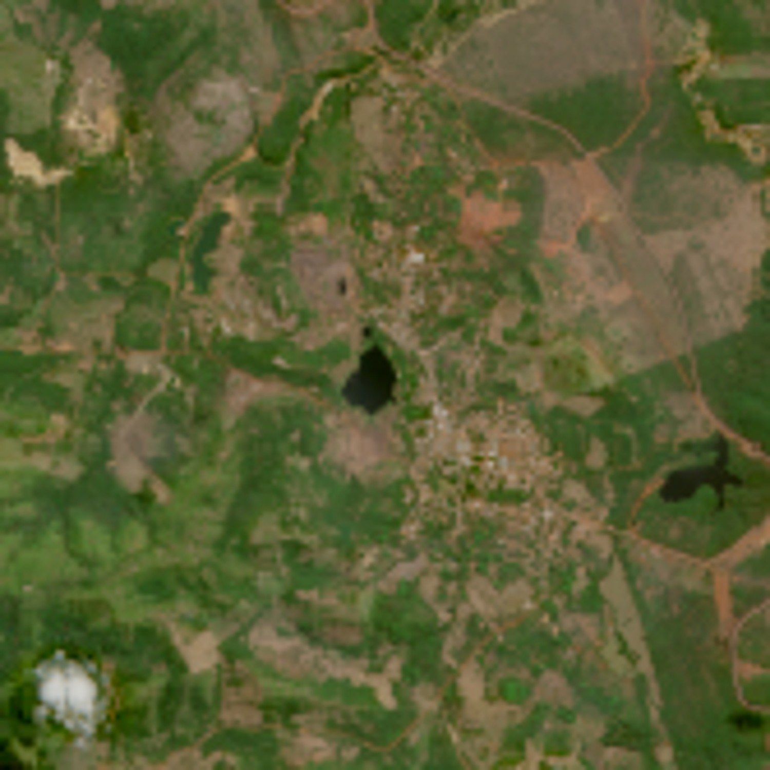 Imagem de satélite da área da cava de Serra Pelada: um lago escuro no centro, cercado por solo exposto e mata, com a vila ao lado